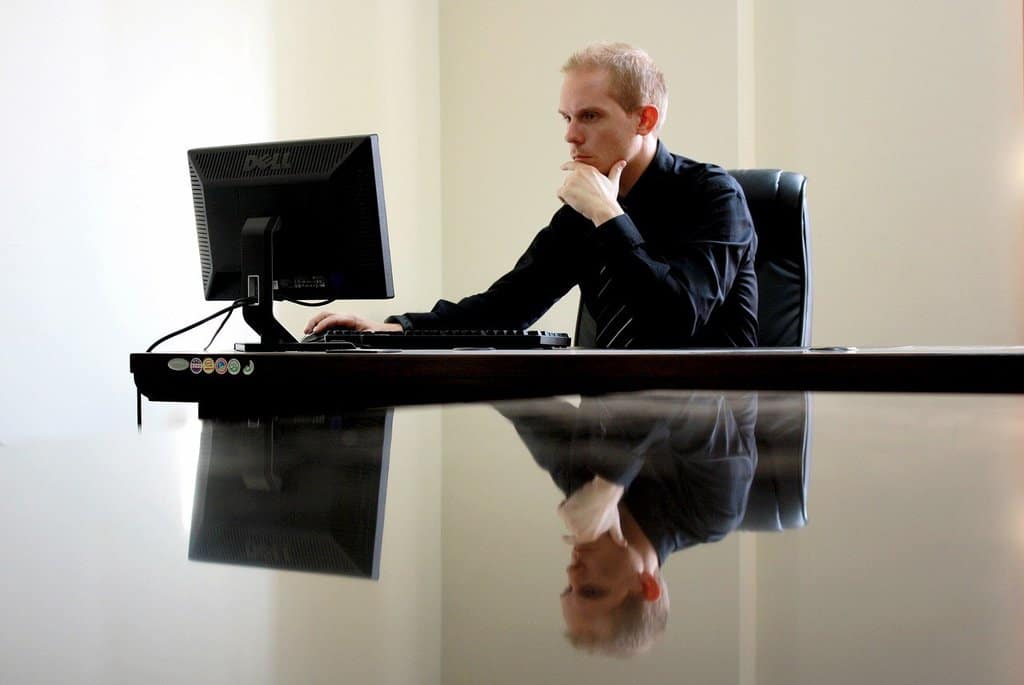 młody mężczyzna siedzący przy biurku, pracujący na komputerze
