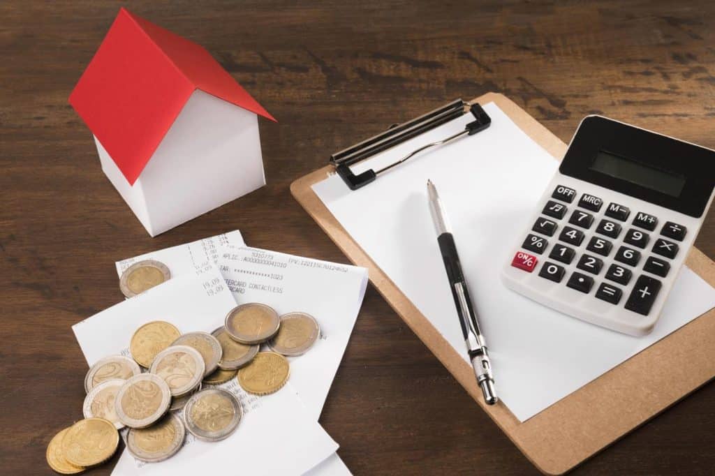 kalkulator na kartce papieru, obok monet i małej makiety domku