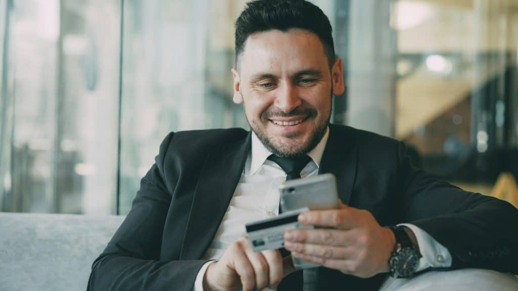 Man in suit smiling while holding phone and credit card