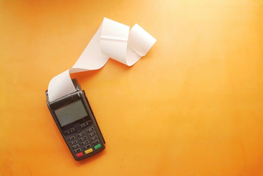 A black payment terminal with a long white paper receipt on orange background